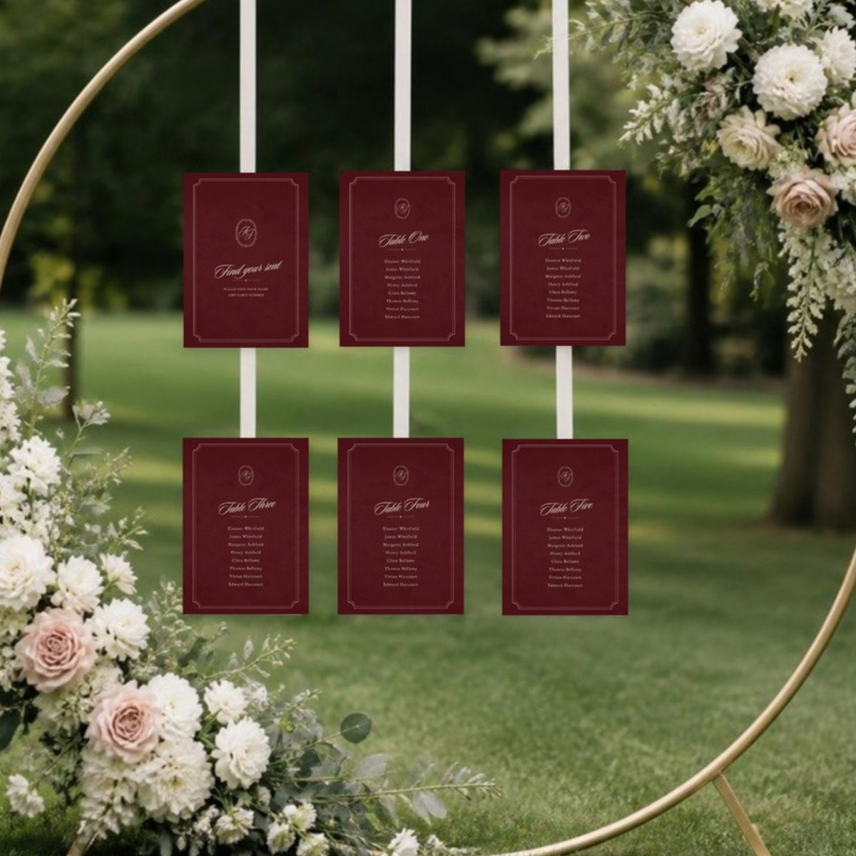 Seating chart cards hung on ribbons from a floral hoop arch on a lawn
