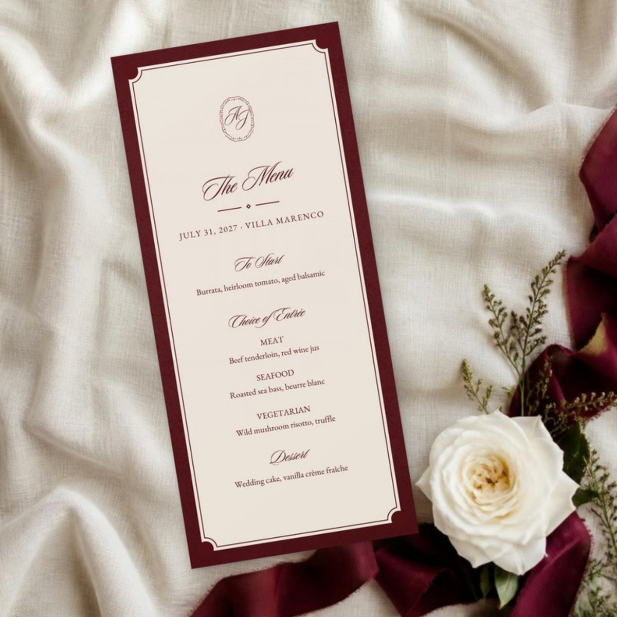 Burgundy-bordered menu card on ivory linen with a white rose and ribbon